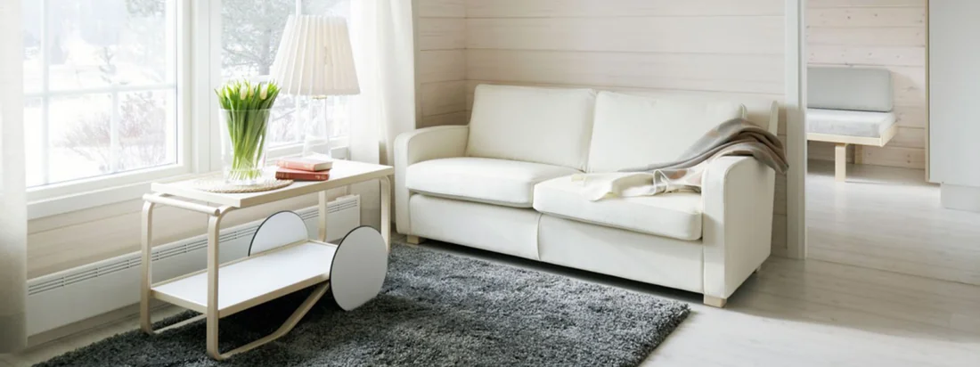 Der Servierwagen 901 von Artek ist der Hingucker in Ihrem Wohnzimmer und noch dazu ein praktischer Beistelltisch. Besonders schön wirkt er im Tageslicht, das durch das Fenster scheint.