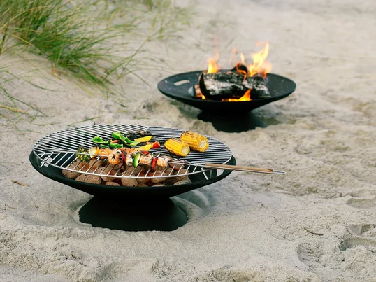 Die Helios Feuerstelle von Skagerak sorgt für eine gemütliche Atmosphäre und Stimmung im Garten. Sie ist aber auch mit dem zugehörigen Edelstahlrost perfekt zum Grillen geeignet.