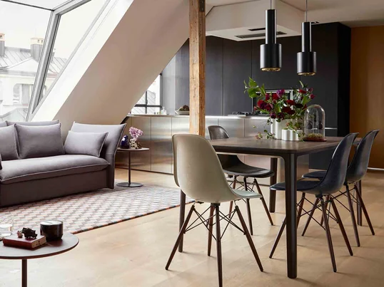 Offene Wohnküche mit Sofa, Küche und dem Esstisch Dining Table von Vitra. Die Eames Fiberglass Stühle von Vitra laden zum Sitzen ein, während die Pendelleuchten mit dem Namen A 110 Handgranate von Artek für gemütliches Licht sorgen.