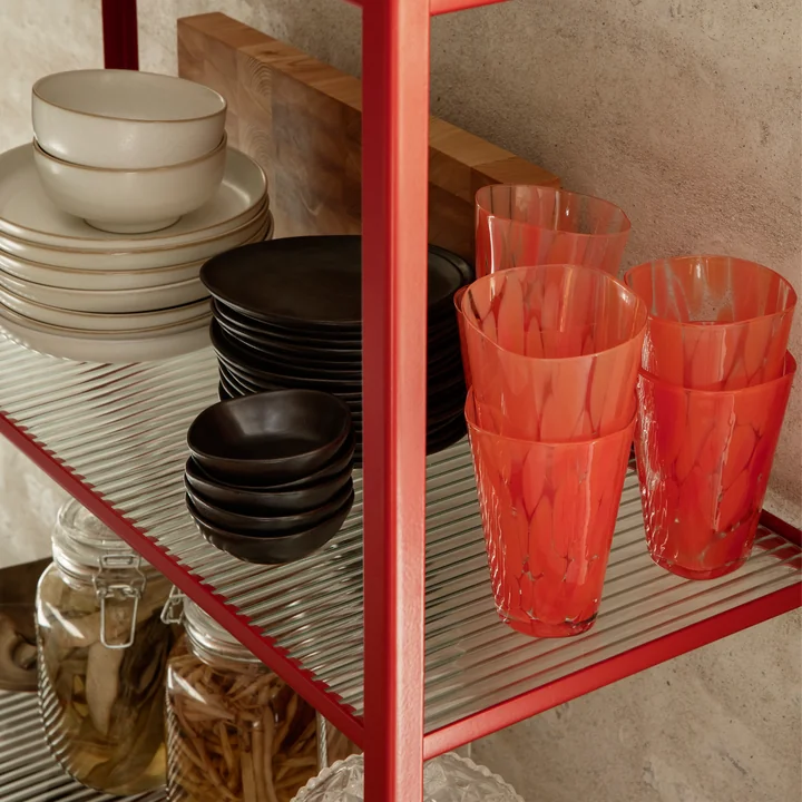 Das Casca Trinkglas von Ferm Living in poppy red in einem Wandregal neben weiterem Geschirr