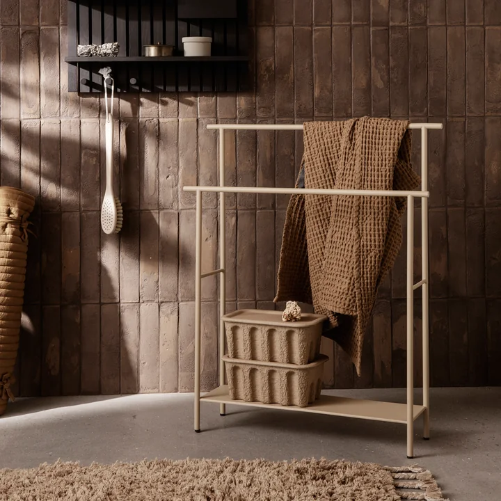 Der Dora Handtuchhalter von Ferm Living mit Handtüchern und Papierboxen neben einem Wandregal