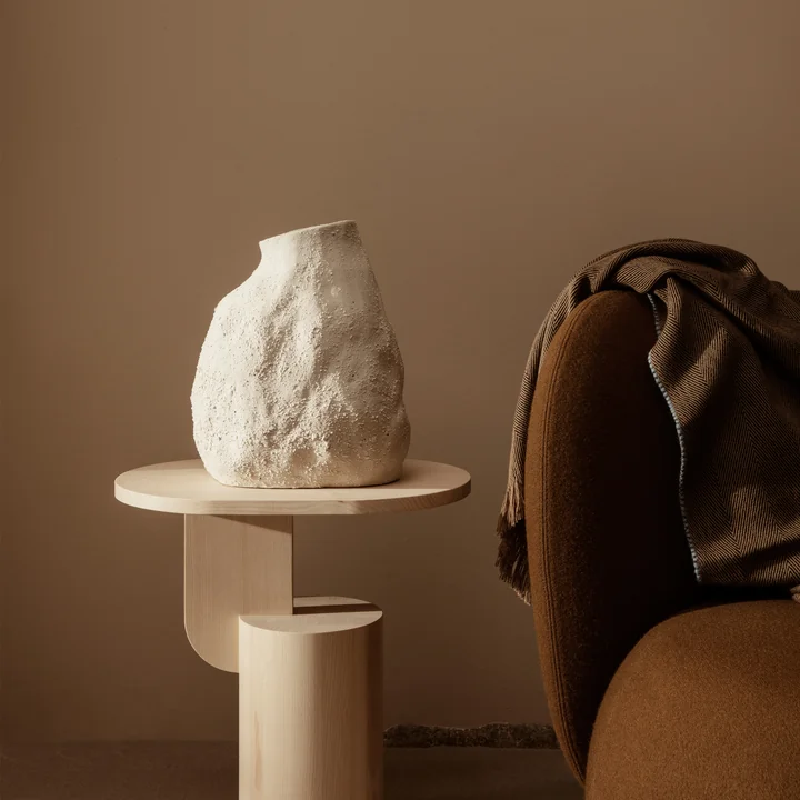 Die Vulca Vase von Ferm Living auf einem Holz-Beistelltisch neben einem braunen Sessel