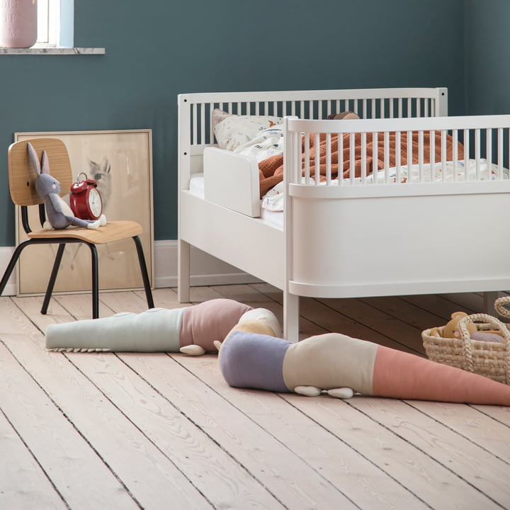Das verspielte Sleepy Croc Kissen von Sebra neben dem weißen Kinderbett