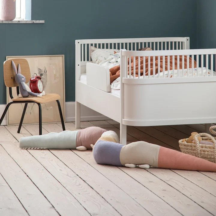Das verspielte Sleepy Croc Kissen von Sebra neben dem weißen Kinderbett