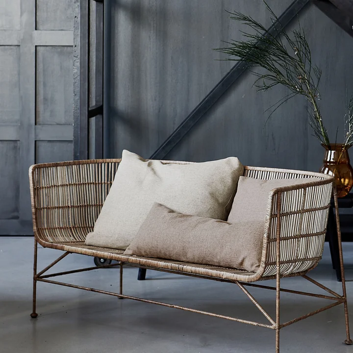 Die Fine Outdoor Kissen von House Doctor auf einer geflochtenen Bank im Innenbereich